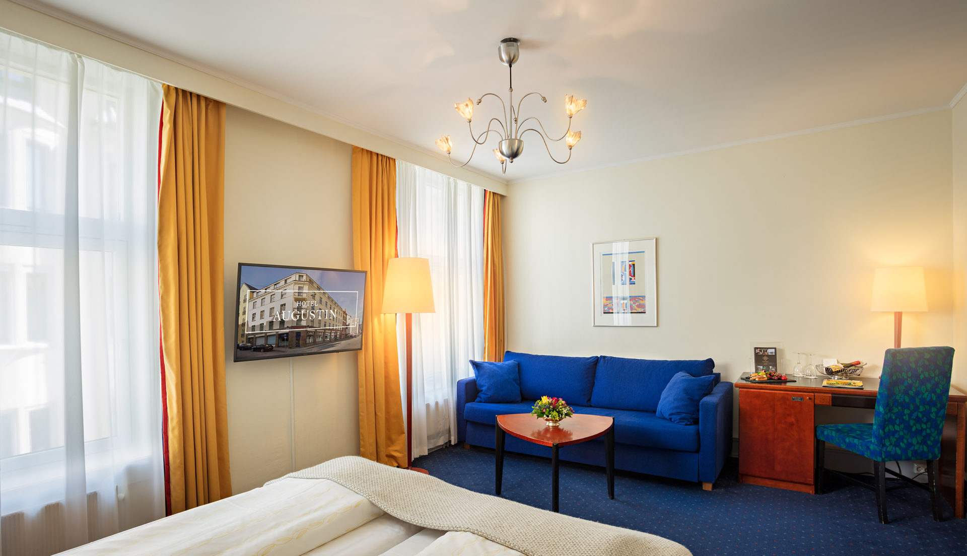 Hotellrom med blå sofa, blått teppe og lyse vegger På Augustin Hotel